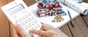 A female hand operating a calculator in front of a Villa house model