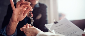 Real estate agent sitting at the desk by the window and passing keys to his client in the office